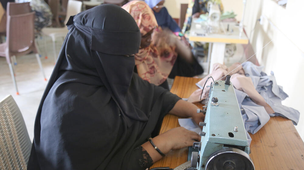  A woman works at a sewing machine in the Women’s Center in Hai Al-Qassam, Ad Damazin, participating in an income-generating workshop. She is learning valuable sewing skills to gain financial independence, while other women in the background are similarly engaged in creating products like school uniforms in a safe, supportive environment.